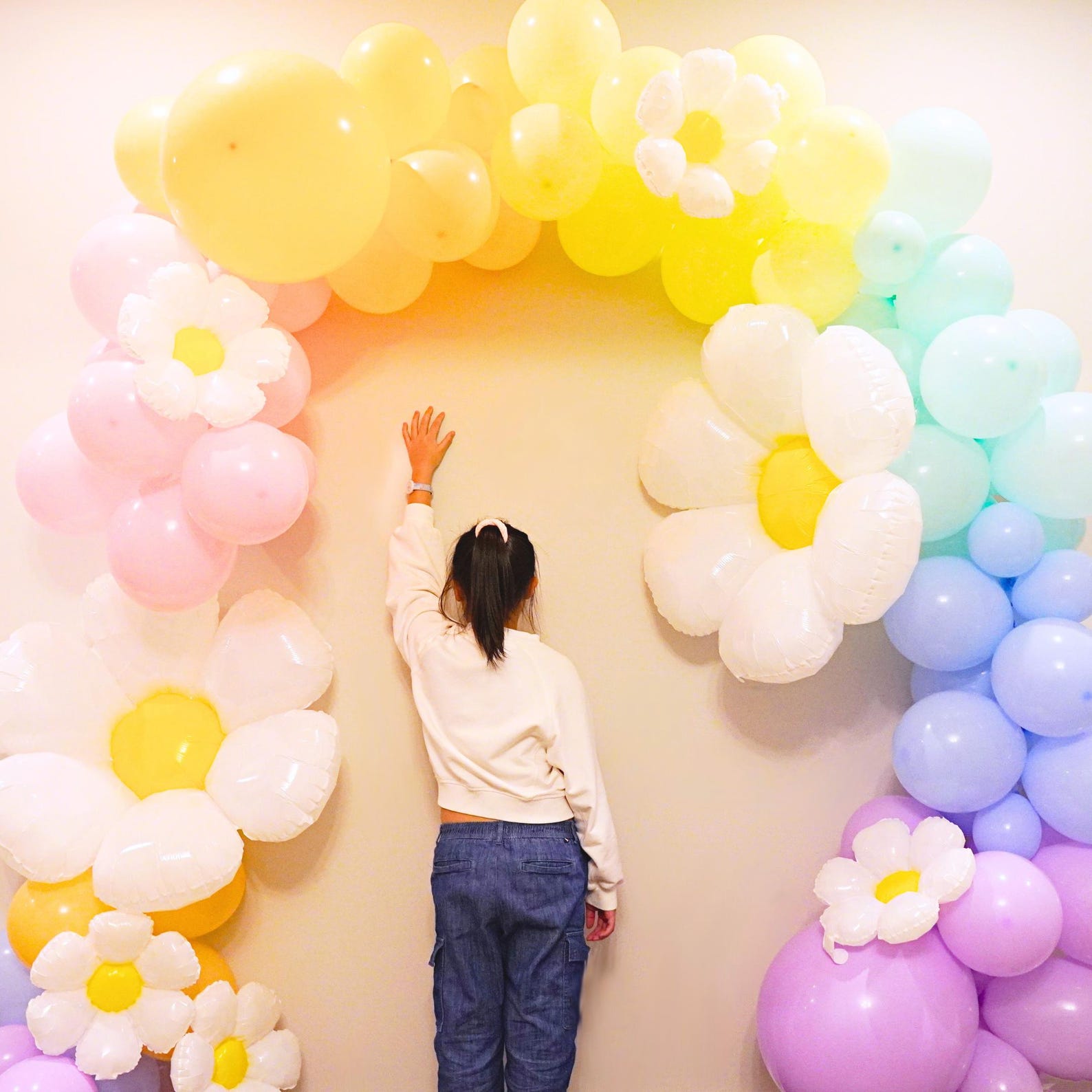 Child next to a pastel daisy balloon arch